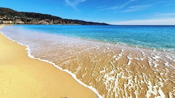 A beach with clear blue water, sandy shore, and a distant mountain range. - Exotic escape - luminous, charming veranda (Bormes-les-Mimosas)