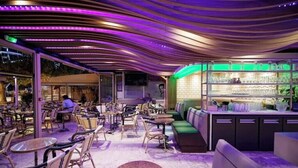 An outdoor seating area with tables and chairs, a bar area with shelves, and a green cushioned seating area. - Exotic escape - luminous, charming veranda (Bormes-les-Mimosas)
