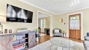 A living room with a flat-screen TV, wooden entertainment unit, glass coffee table, and a cozy seating area.