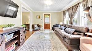 A living room with a leather sofa, a glass coffee table, a TV mounted on the wall, and a wooden entertainment unit.