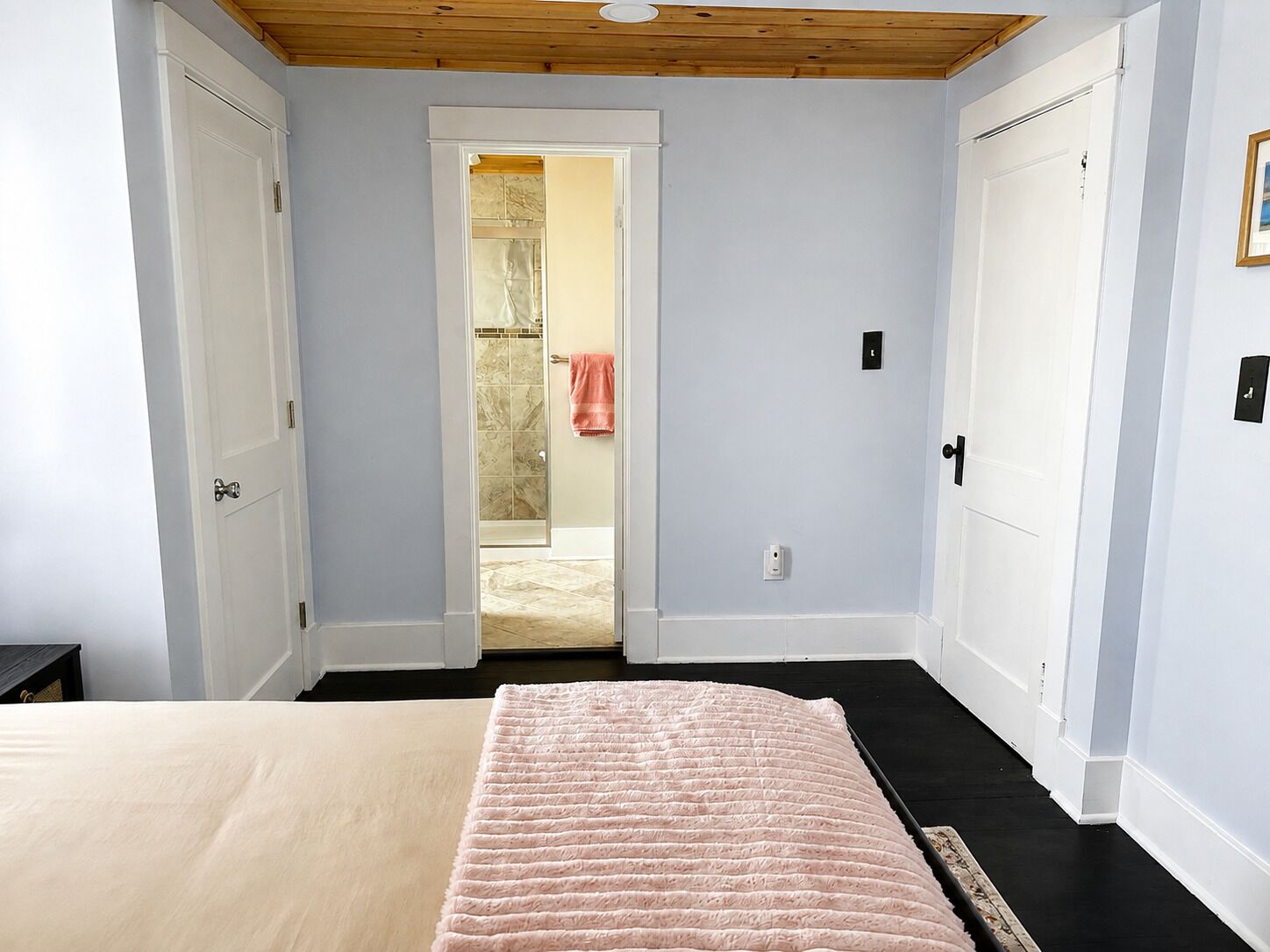 A bedroom with a bed, a door leading to a bathroom, and a wooden ceiling.