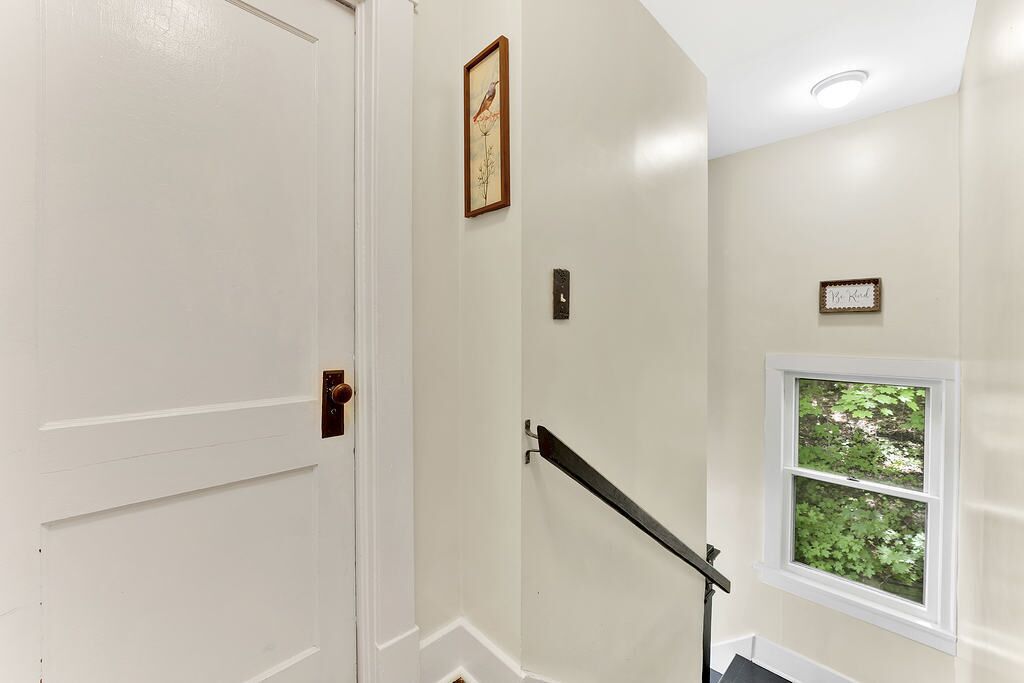 A staircase with a handrail, a door, and a window with a view of greenery.