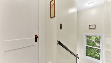 A staircase with a handrail, a door, and a window with a view of greenery.
