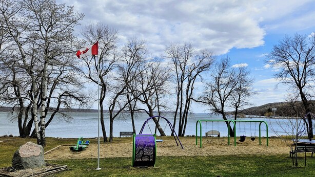 Un parque con un área de juegos, una bandera y un lago.