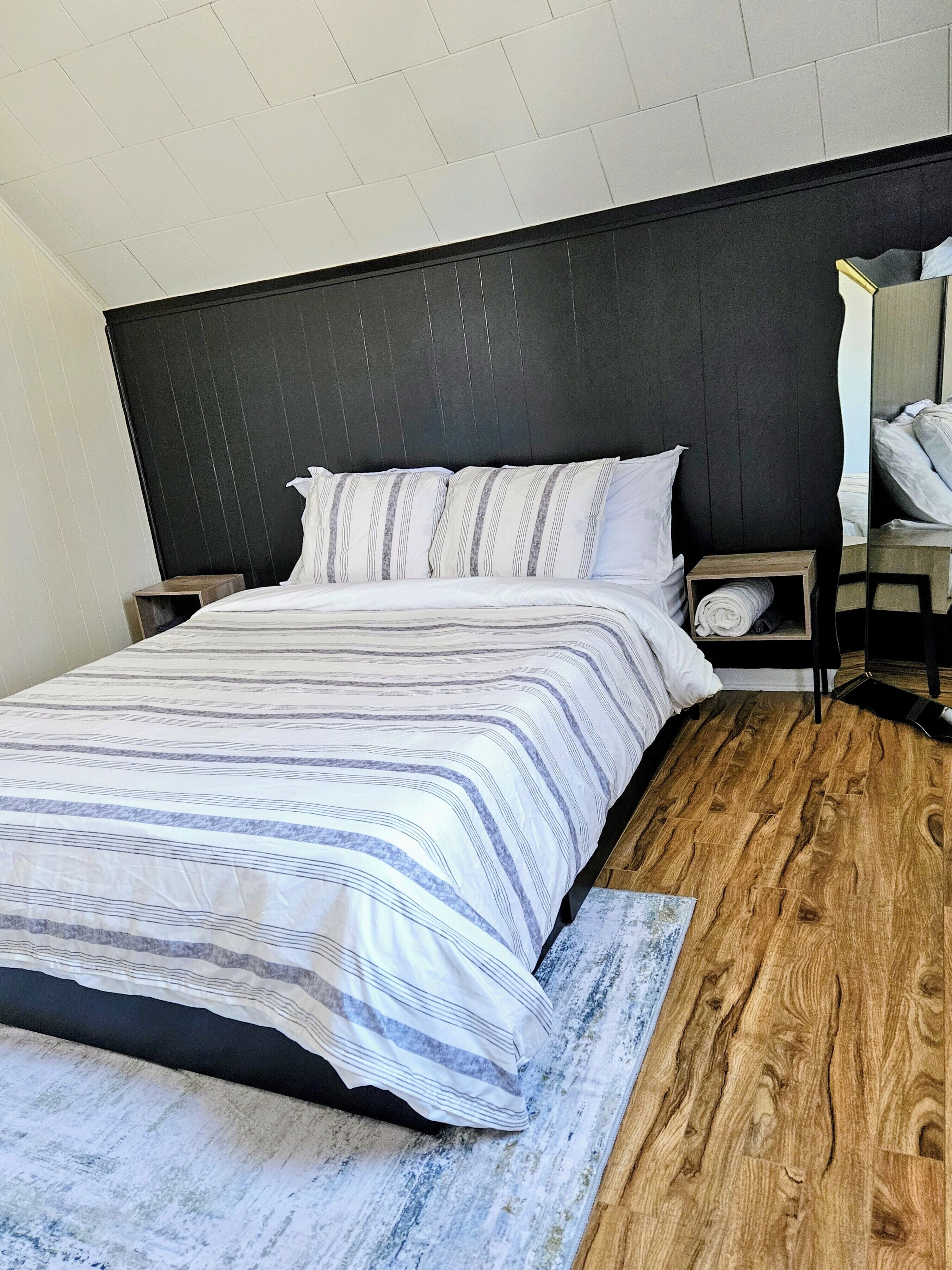 Un dormitorio con una cama grande, suelo de madera, cabecera oscura y una mesita de noche con lámpara.