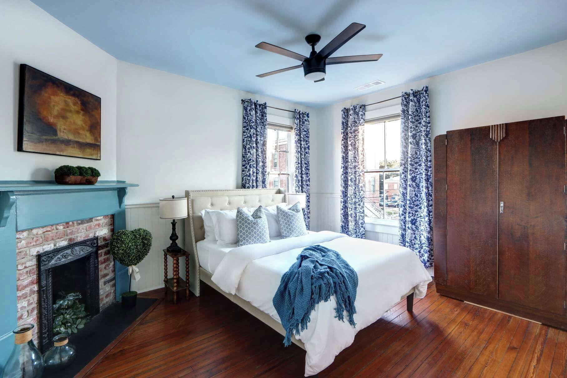 A bedroom with a bed, a fireplace, a ceiling fan, and a large wardrobe.