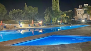 Un área de piscina nocturna con sillones de descanso y sombrillas.