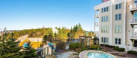 Un immeuble à plusieurs étages doté d’un espace piscine, entouré d’arbres et surplombant un ciel dégagé.