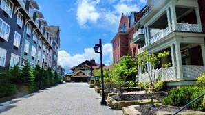 A paved walkway flanked by multi-story buildings with balconies, a clear sky, and a distant building with a red roof. - Ski In Ski Out Top Floor 2 BR Seneca Corner Unit. Newly Renovated-Garage Parking (Snowshoe)