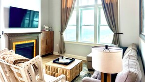 A living room with a fireplace, a television, a sofa, a lamp, and a view of the outdoors. - Ski In Ski Out Top Floor 2 BR Seneca Corner Unit. Newly Renovated-Garage Parking (Snowshoe)