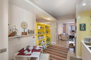 A hotel room with a dining area, a yellow bookshelf, a kitchen area, and a bed.