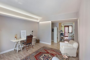 Een moderne woonkamer met een wit bureau, een kamerbreed tapijt, een witte bank en uitzicht op een andere kamer met een keuken.