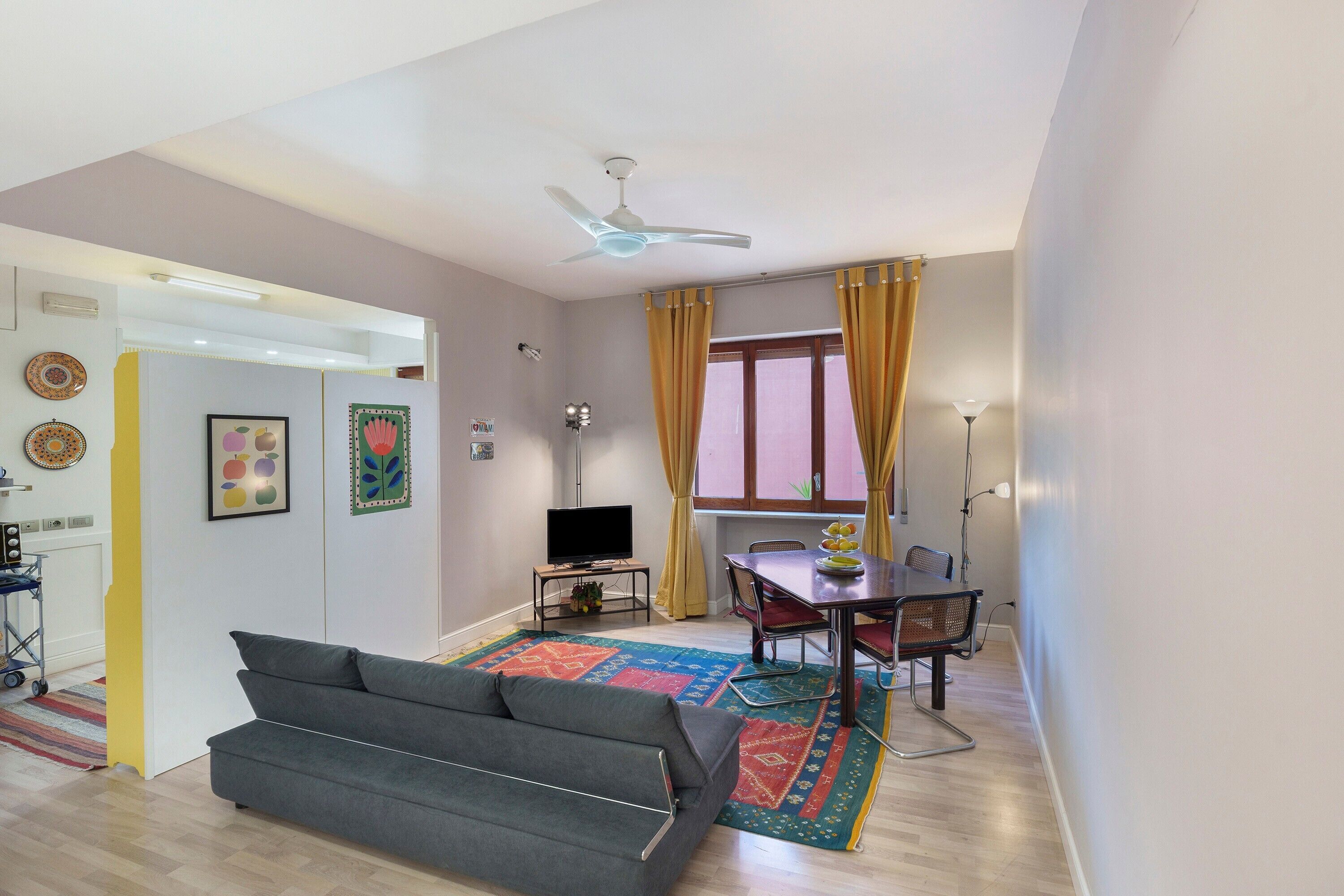A living room with a sofa, a dining table with chairs, a television, and a ceiling fan.