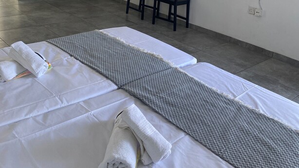 Ein Hotelzimmer mit Bett, einem kleinen Tisch mit Stühlen, einem an der Wand befestigten Fernseher und einer Küchenzeile im Hintergrund.