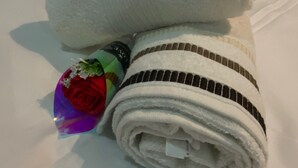 Ein ordentlich gefaltetes weißes Handtuch mit Streifenmuster, ein zusammengerolltes Handtuch und ein Strauß roter Rosen auf einem Bett mit weißen Kissen.