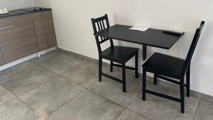 Eine kleine Küche mit einem dunklen Holztisch und Stühlen, einer weißen Fliesenrückwand und einem grauen Fliesenboden.