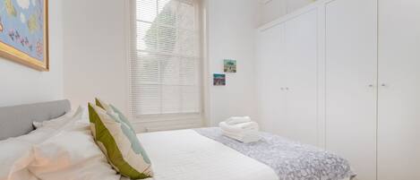 A bedroom with a bed, a window with blinds, a wardrobe, and a painting on the wall.