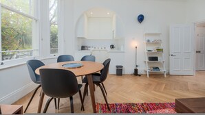 A modern kitchen with white cabinets, a round wooden table, and blue chairs. - Quirky Hampstead Flat RH6 (London)