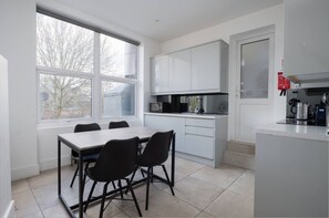 A modern kitchen with white cabinets, a dining table with chairs, and a large window providing a view of the outside. - Stunning London Home - Newly Furnished Mhb352 (London)