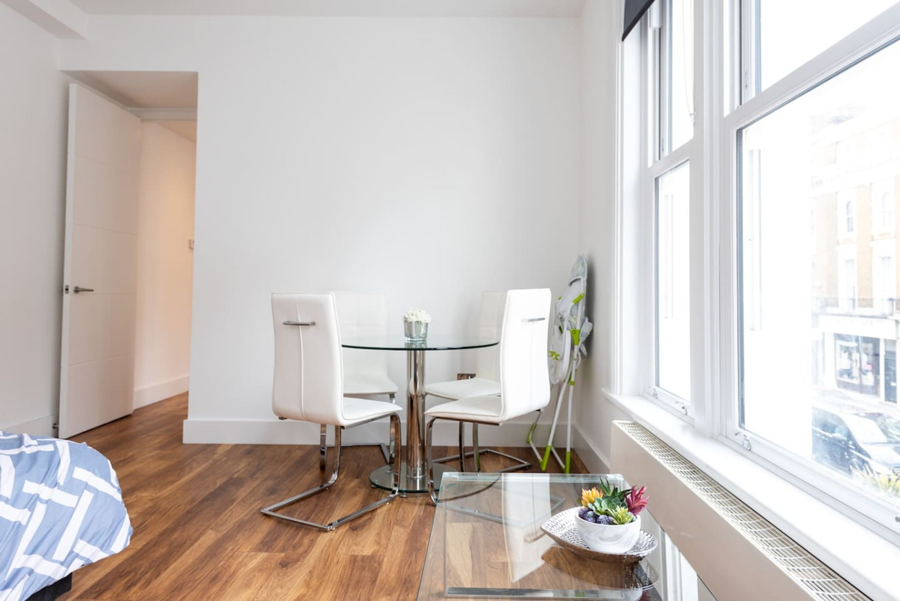 A modern room with a glass table, white chairs, a small plant, and a window with a city view.