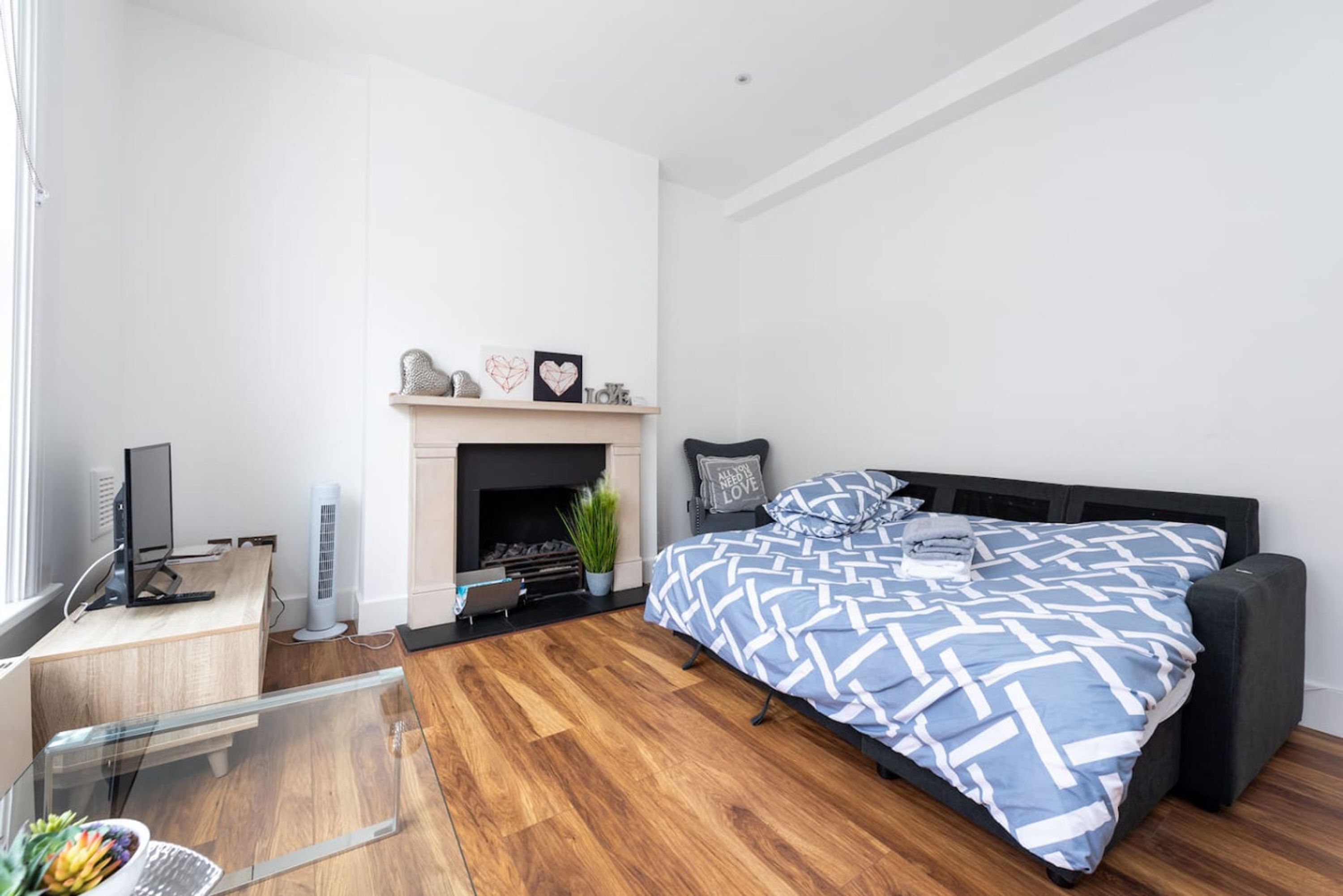 A bedroom with a bed, a desk, a fireplace, and a window.