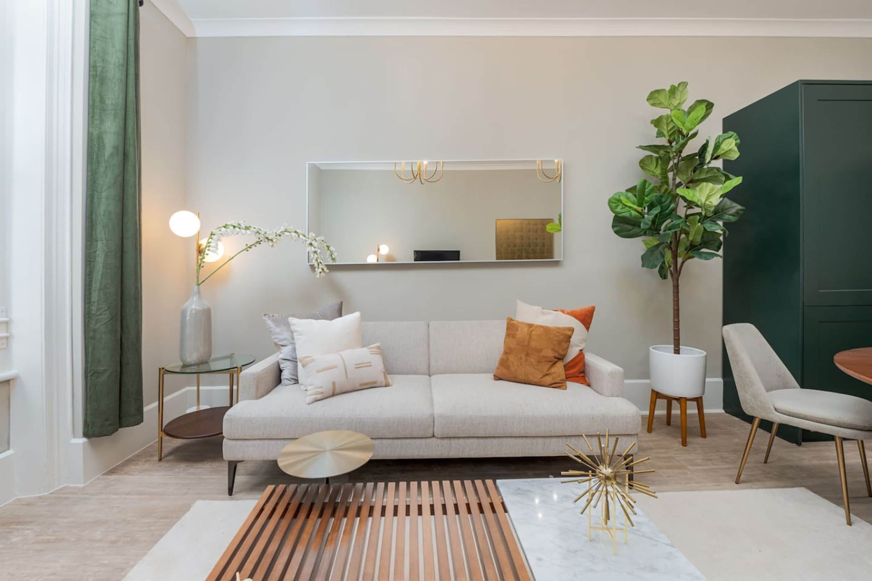 A modern living room with a sofa, a coffee table, a side table, a mirror, a plant, and a chair.