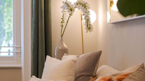 Ein Sofa mit mehreren Kissen, eine Vase mit Blumen und ein Spiegel mit Beleuchtung.