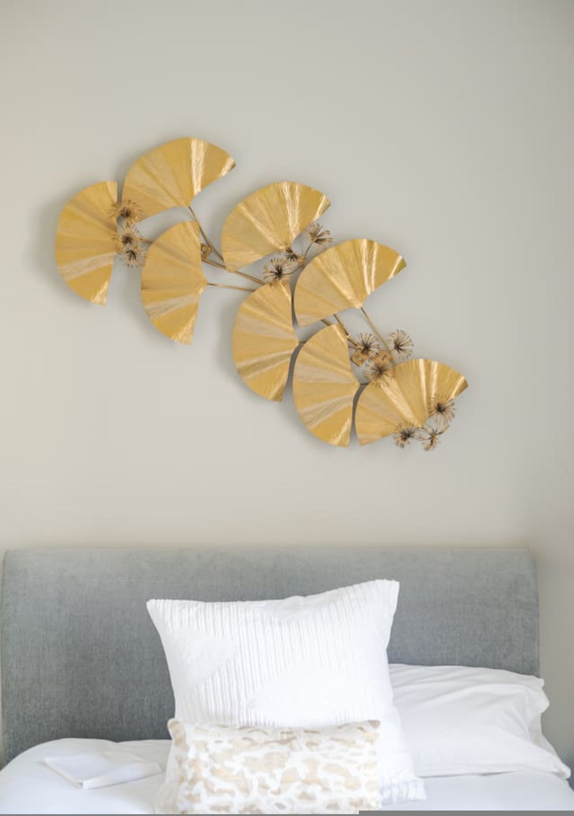 A bed with white bedding and a gray headboard, a white pillow, and a decorative wall piece with gold and white elements.