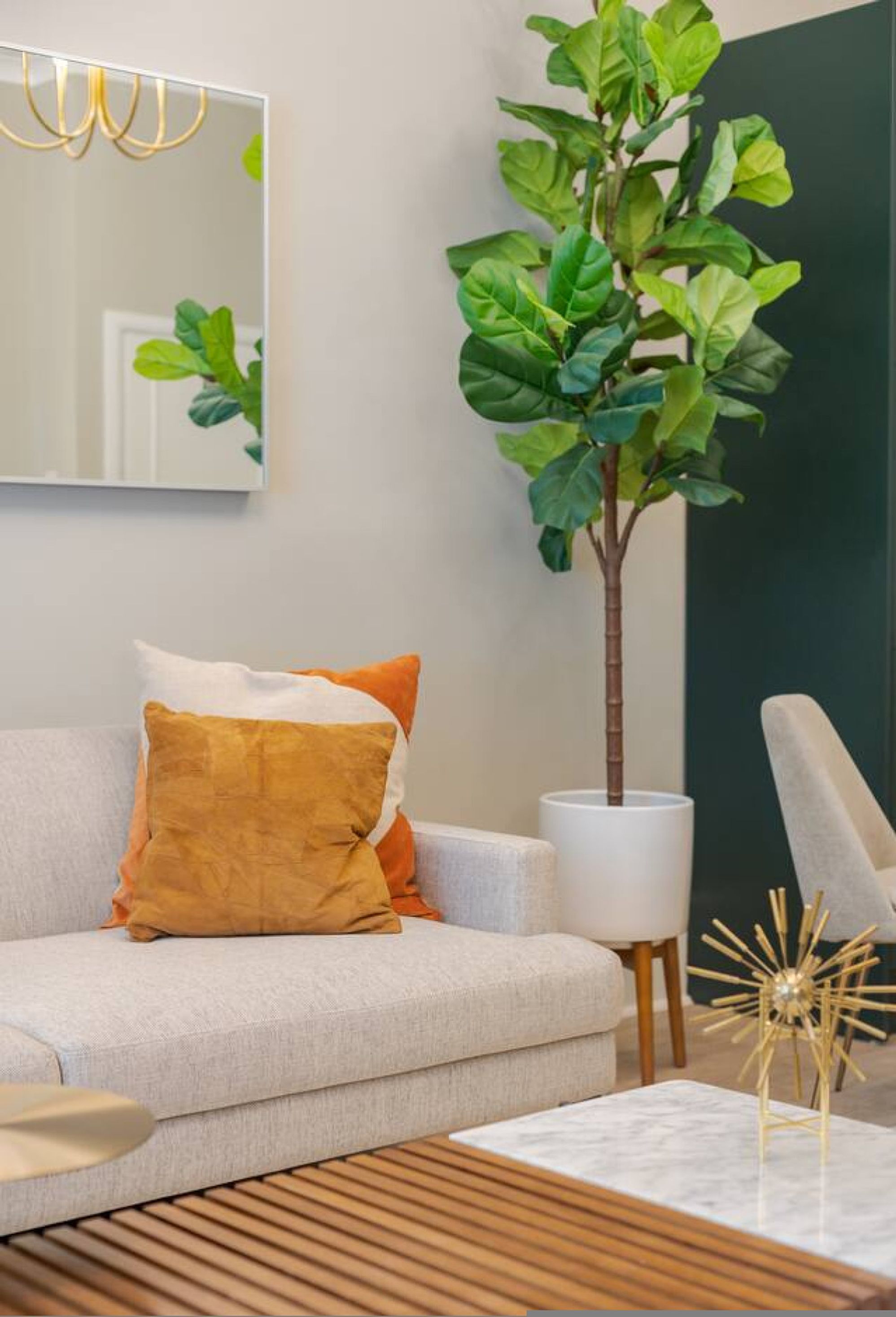 Una sala de estar moderna con sofá, cojines, una planta en maceta, una lámpara y un objeto decorativo sobre una mesa de centro.