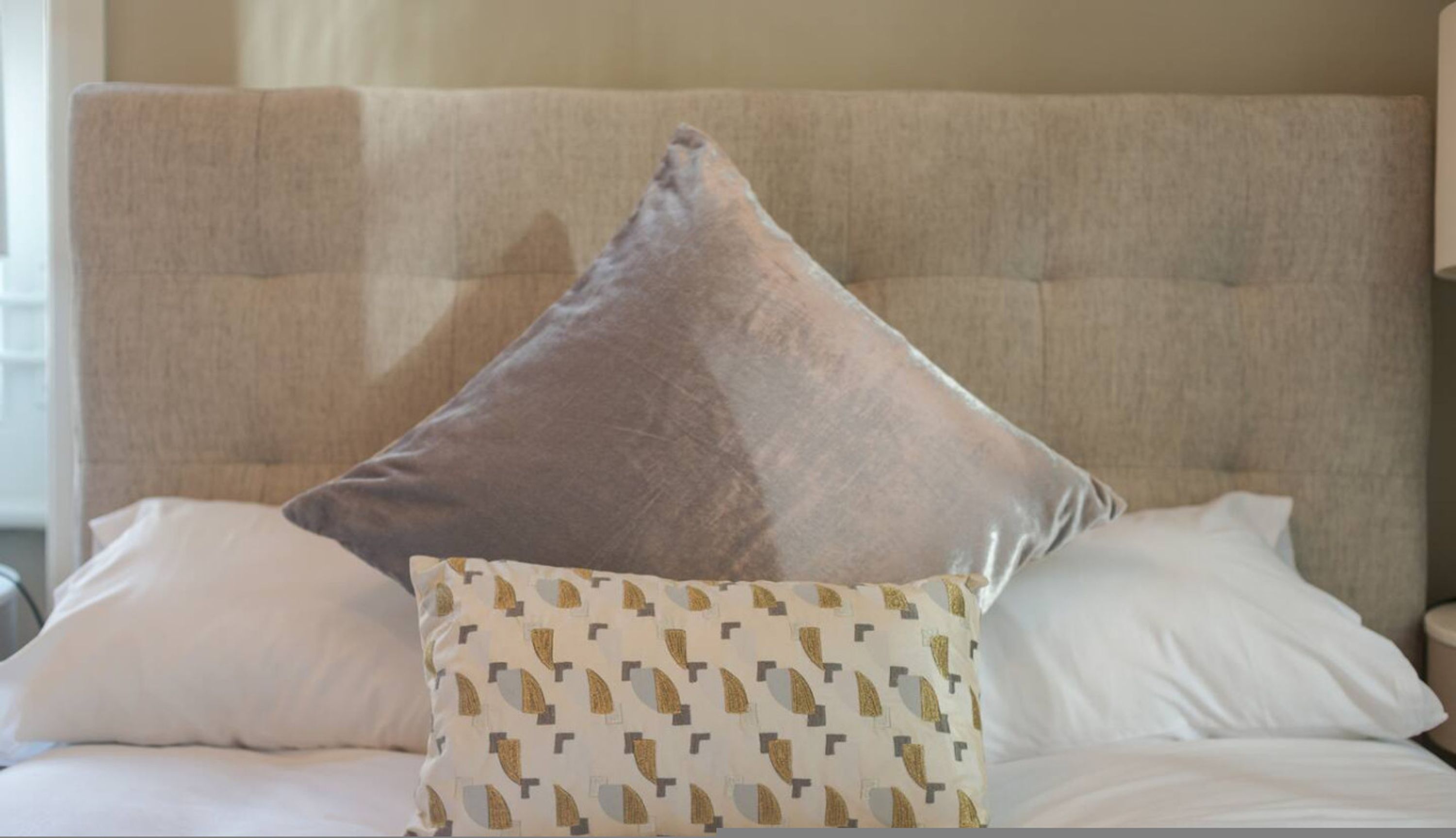 A bed with a tufted headboard, a large square pillow, and a patterned pillow.