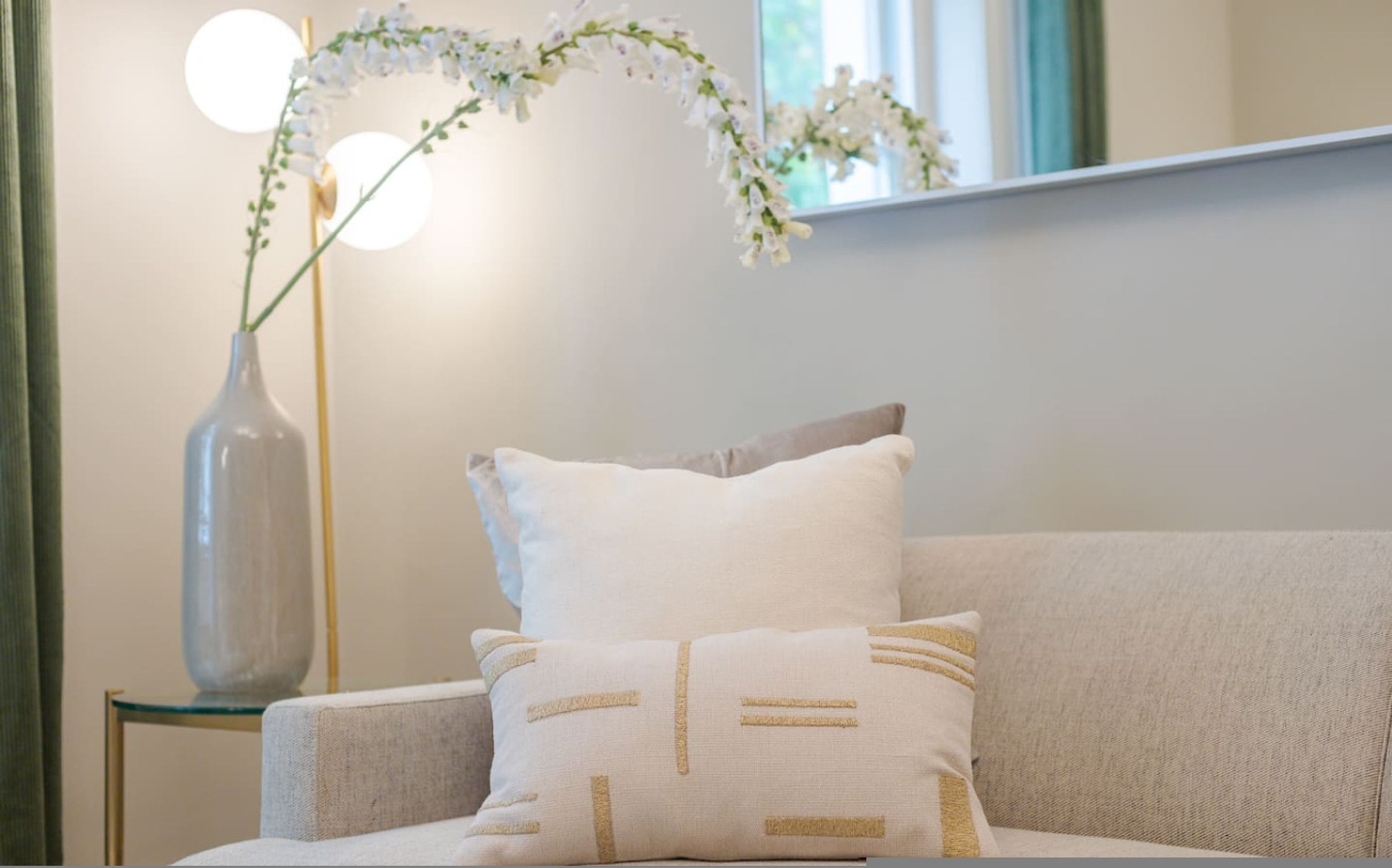 Un canapé avec deux coussins, un vase avec des fleurs et une lampe sur pied.