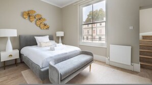 Ein Schlafzimmer mit Bett, Nachttischlampen, einer Bank, einem Fenster und einer Heizung.
