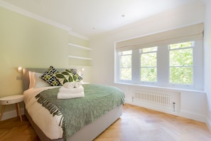 Ein Schlafzimmer mit einem Bett, einem Fenster mit Blick auf Grünflächen, einem Heizkörper und einem Nachttisch.