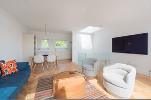 Ein modernes Wohnzimmer mit einer Couch, Sesseln, einem Couchtisch und einem an der Wand befestigten Fernseher.