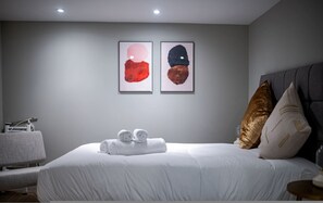 Une chambre moderne avec un lit bien fait, deux tableaux abstraits encadrés accrochés au mur et une petite table de chevet avec une lampe.