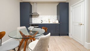 A compact kitchen with dark cabinets, a marble backsplash, and a glass dining table with chairs. - Gorgeous Apartment by the Park PS6 (London)