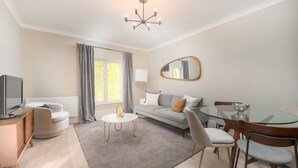 A modern living room with a sofa, a glass dining table, and a TV. - Gorgeous Apartment by the Park PS6 (London)