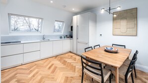 A modern kitchen with white cabinets, a wooden herringbone floor, and a dining area with a wooden table and chairs. - Beautiful Hampstead Home RH9 (London)