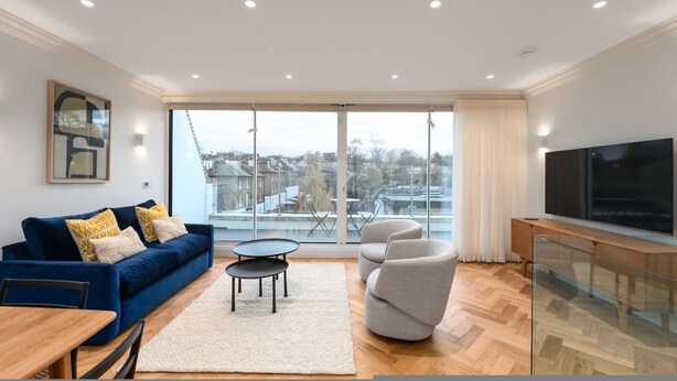 A modern living room with a blue sofa, a glass coffee table, and a TV on a wooden cabinet. - Beautiful Hampstead Home RH9 (London)