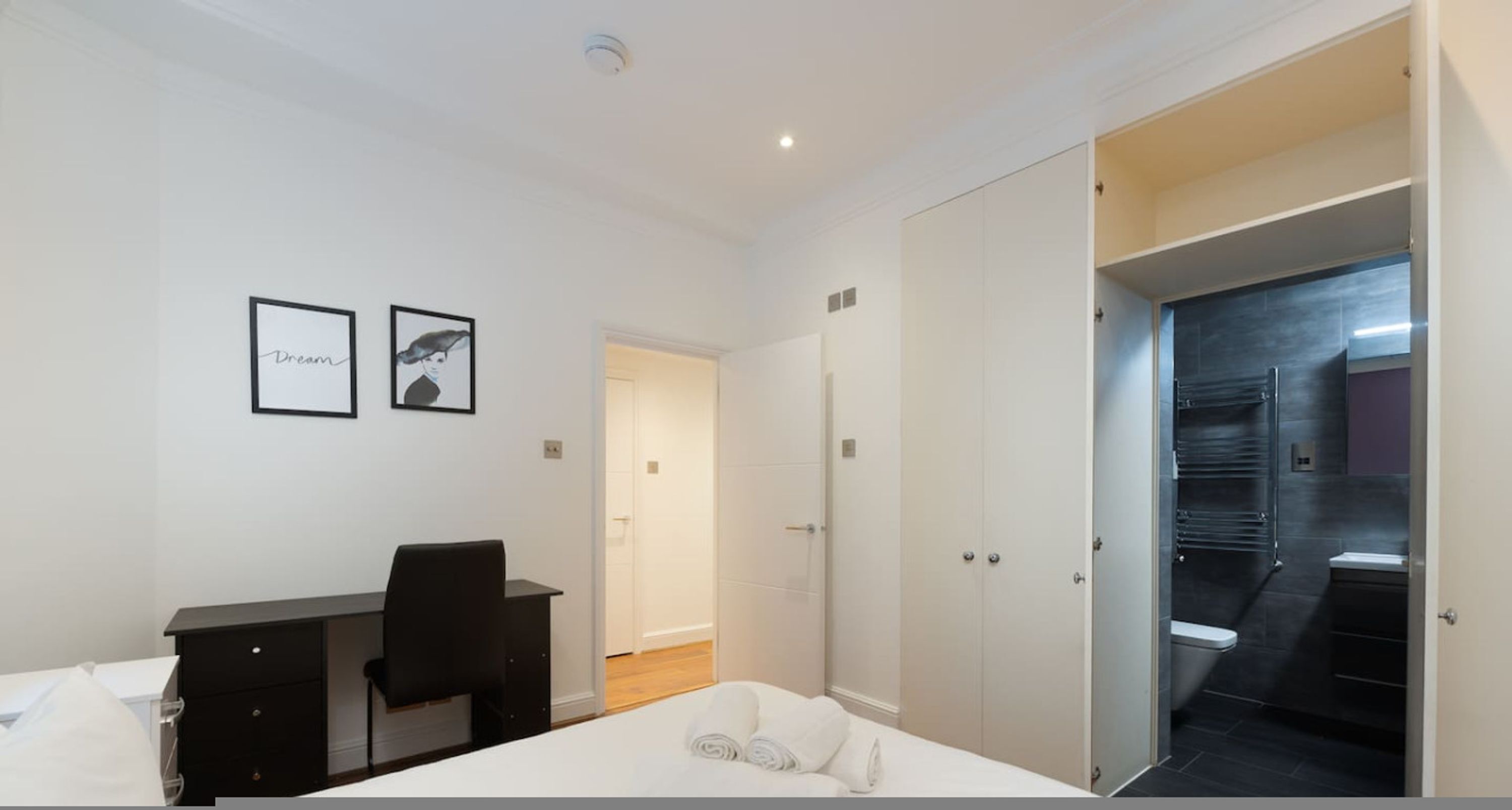 A modern hotel room with a bed, desk, and wardrobe.