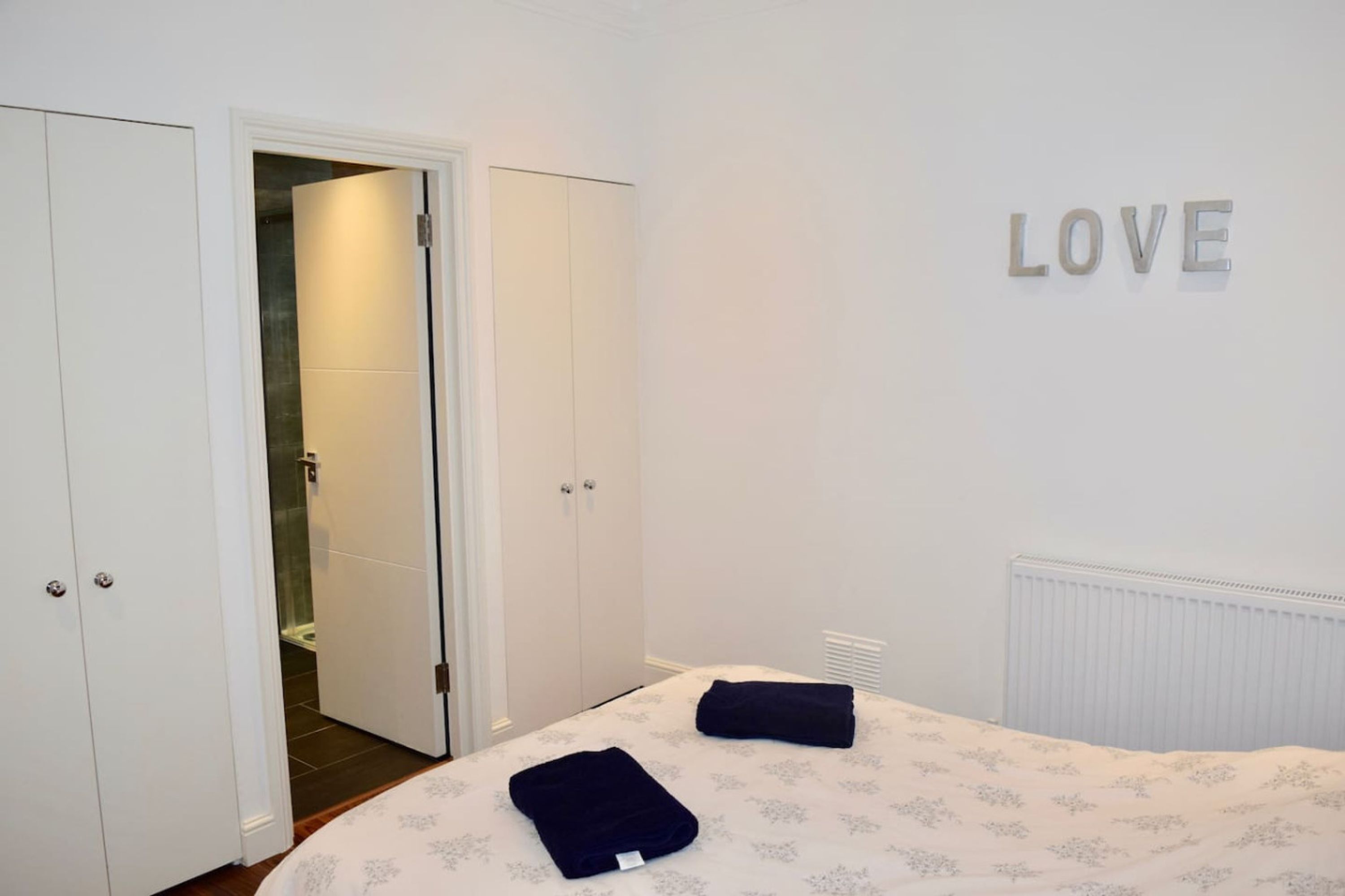 Un dormitori amb llit, dues tovelloles, un armari i una paret amb la paraula 'LOVE'.