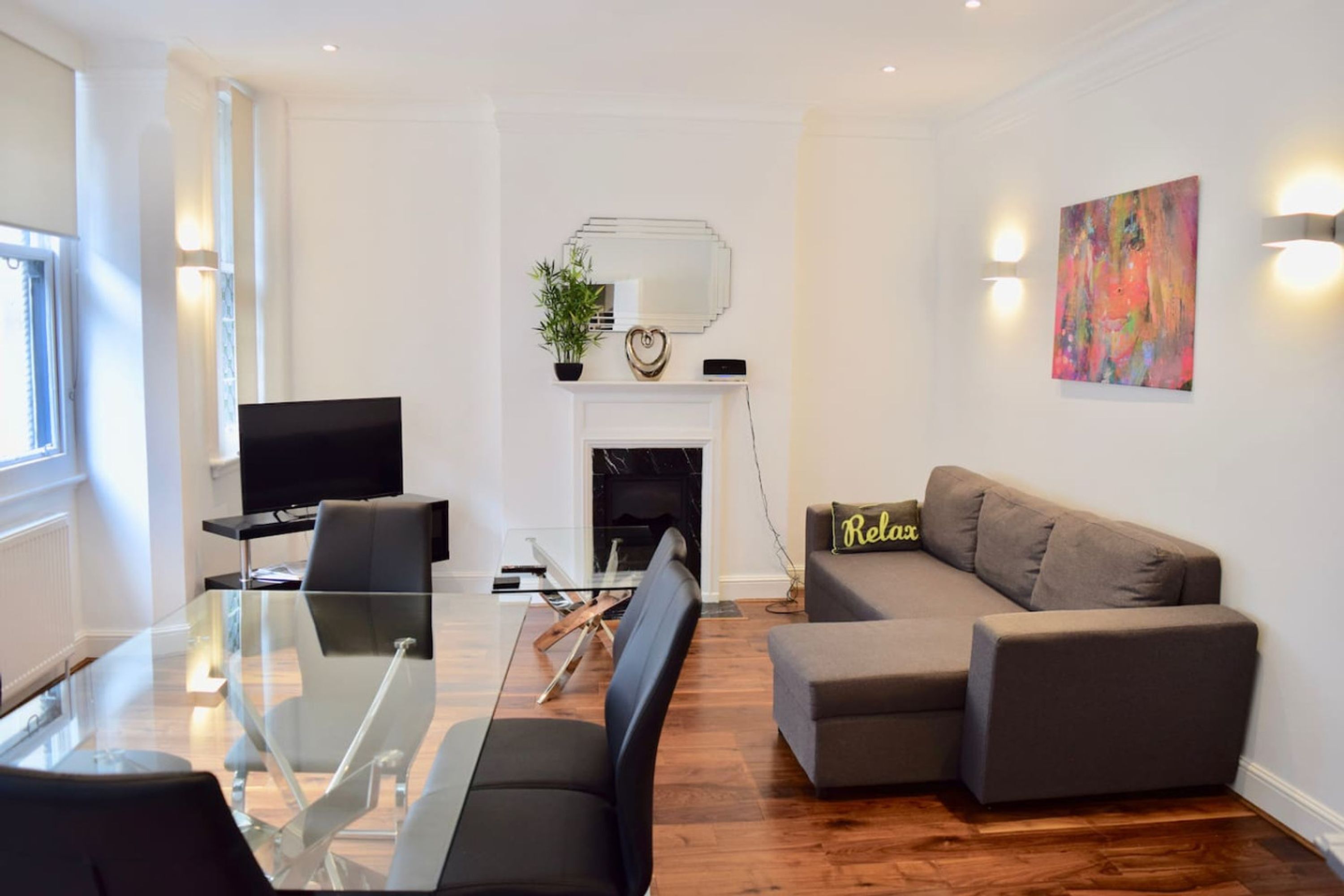 A modern living room with a glass dining table, a sofa, a TV, and a fireplace.