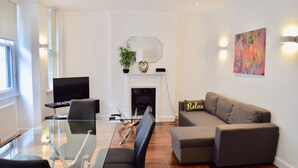 Una sala de estar moderna con una mesa de comedor de vidrio, un sofá, un televisor y una chimenea.