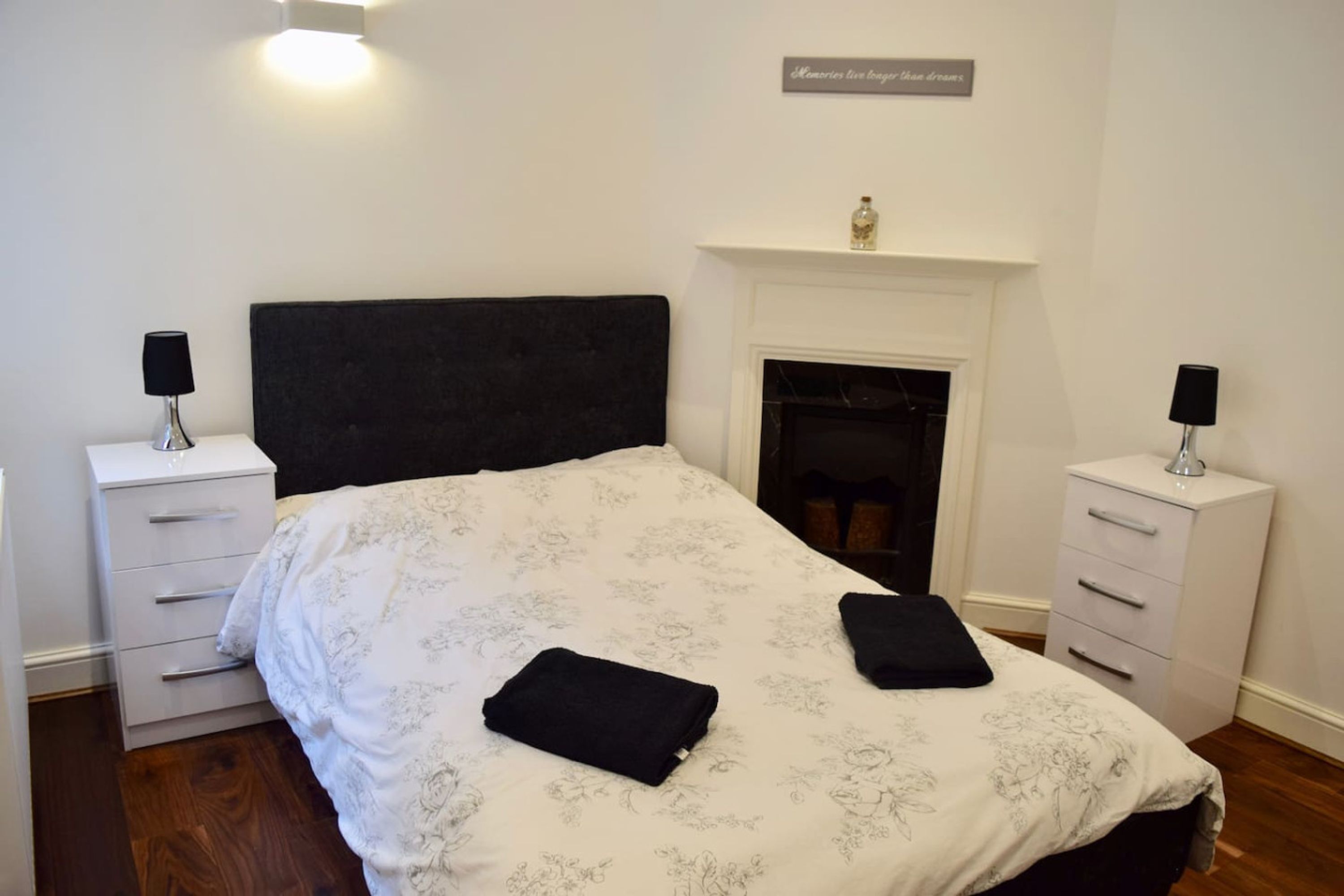 Quarto com cama grande, duas mesas de cabeceira, lareira e placa na parede.