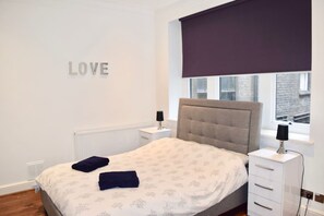 A bedroom with a bed, a nightstand, a window with a view, and a wall with the word "LOVE" on it. - Beautiful Central London Apartment FS2 II (London)