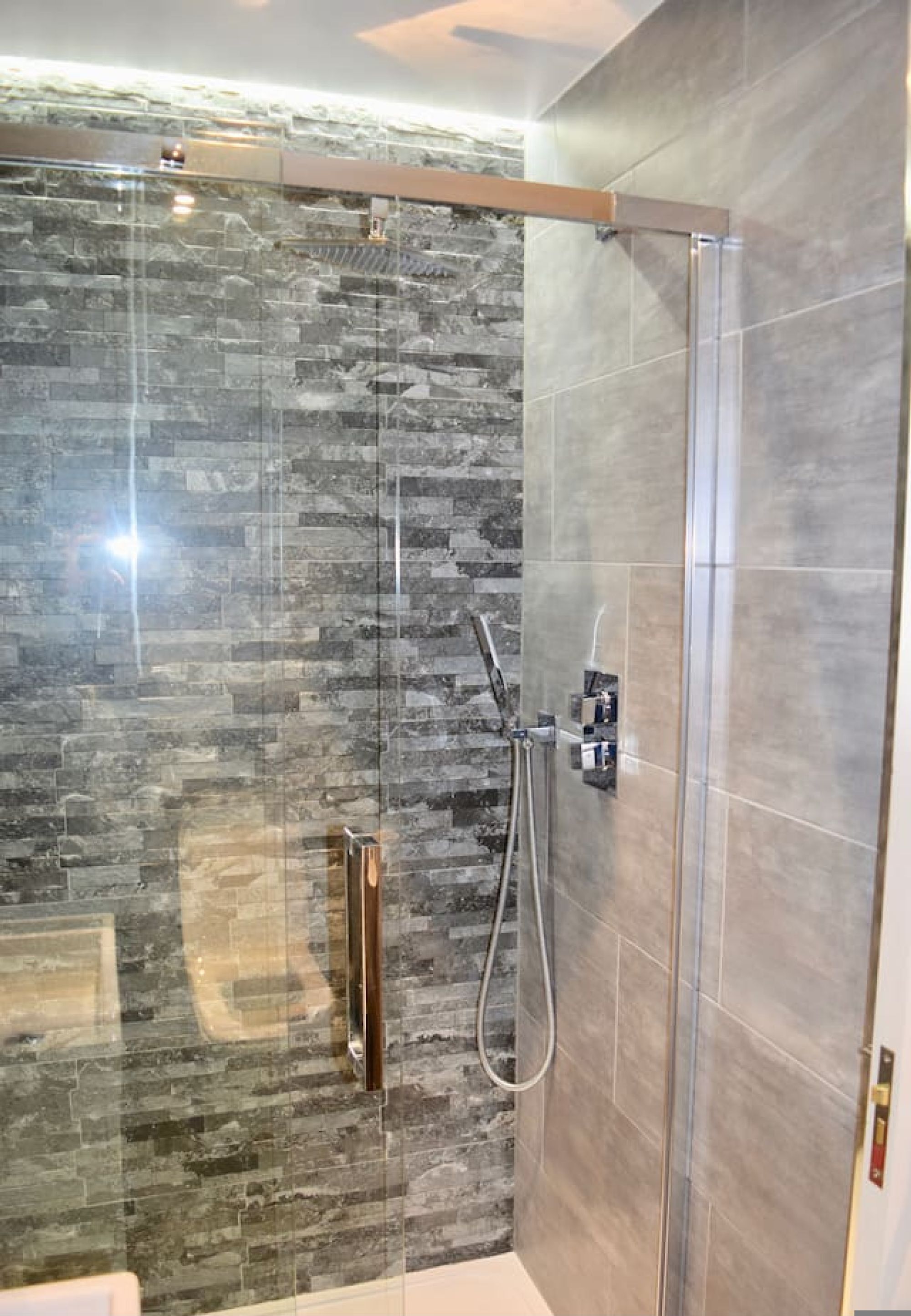 A modern shower with a glass door, a handheld showerhead, and a wall-mounted control panel.