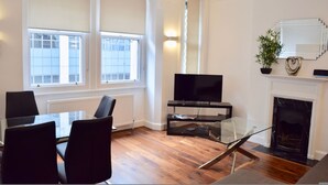 Una sala de estar moderna con chimenea, televisor y comedor con sillas y una mesa de vidrio.