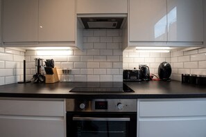 A modern kitchen with white cabinets, a black countertop, and a built-in oven. - Stunning Hyde Park Apartment SS3 (London)