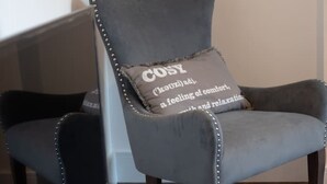 Ein grauer Sessel mit Kissen, auf dem das Wort 'COZY' steht und eine Definition abgebildet ist, neben einem Glastisch mit Zeitschriften.