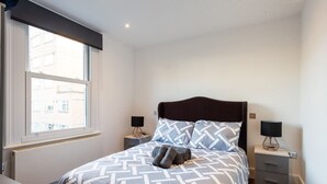 Ein ordentlich eingerichtetes Schlafzimmer mit einem großen Bett, zwei Nachttischen und einem Fenster mit Blick auf Gebäude.